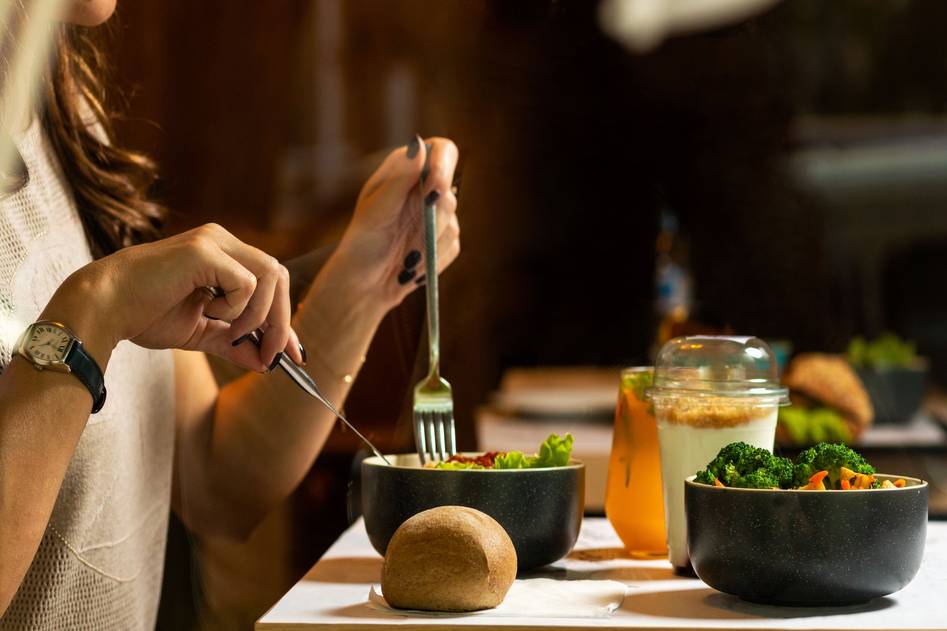 Woman sipping warm herbal soup while holding a skincare journal beside fresh produce